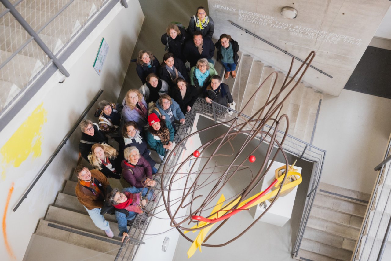 Das Bild zeigt aus der Vogelperspektive eine Gruppe von Teilnehmenden, die im Treppenhaus des K&uuml;nstlerhauses Hannover nach oben zum Fotografen schauen.