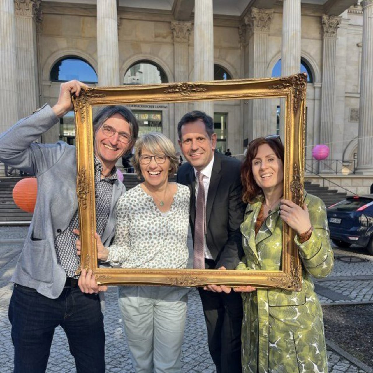 Das Bild zeigt Ministerpr&auml;sident Olaf Lies gemeinsam mit drei Vorstandsmitgliedern von akku. Die Gruppe steht vor dem nieders&auml;chsischen Landtag und h&auml;lt einen gro&szlig;en, goldenen Bilderrahmen in den H&auml;nden, durch das die Personen blicken, um ein feierliches Hochzeitsfoto zu symbolisieren. Von links nach rechts: J&ouml;rg Kowollik, Anja Kr&uuml;ger, Olaf Lies und Vera L&uuml;deck