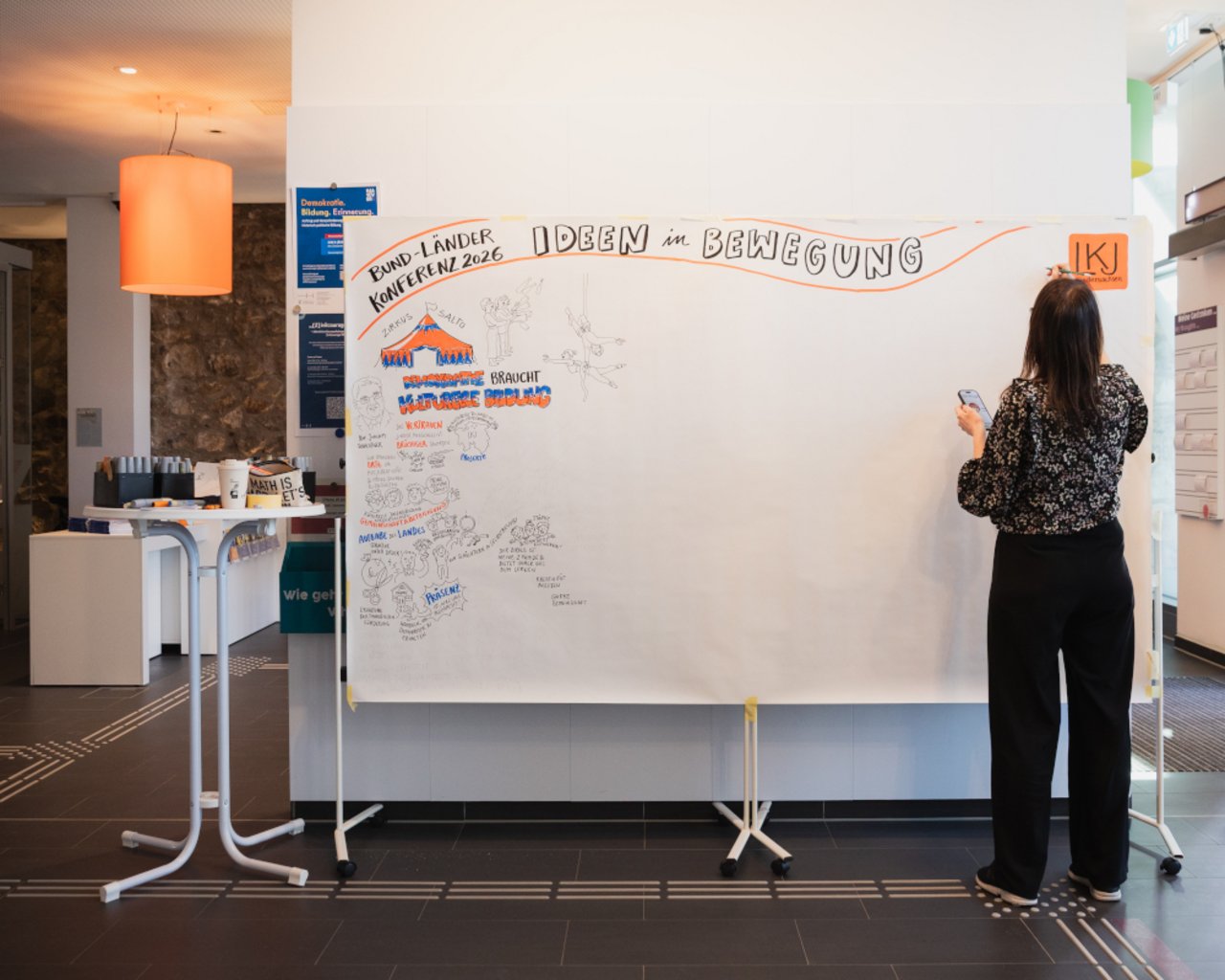 Auf dem Foto ist eine gro&szlig;e Leinwand zu sehen, auf der Barbara Scheider die Ereignisse der zwei Tage durch ein Graphic Recording bildhaft festh&auml;lt.